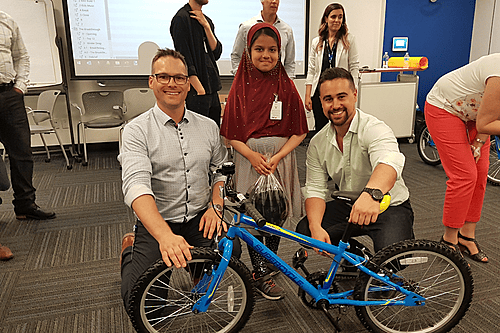 Two corporate team building participants kneeling with a young girl and her new bicycle during a LEVEL 12 philanthropic event.